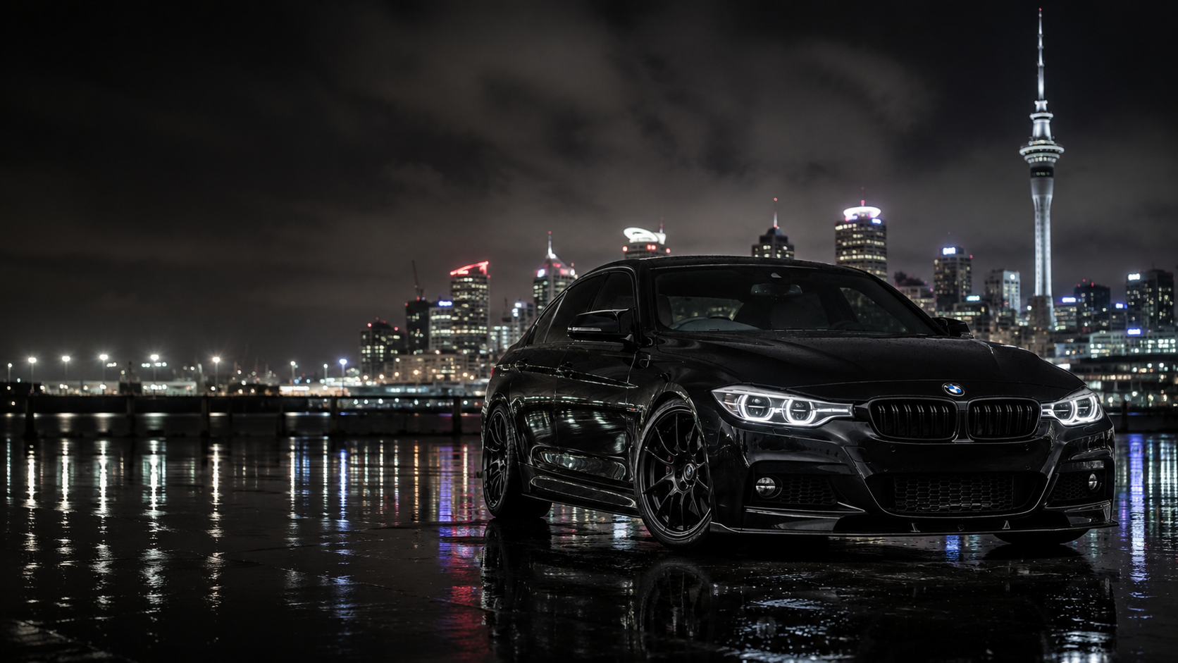 Black European performance car against the Auckland skyline at night